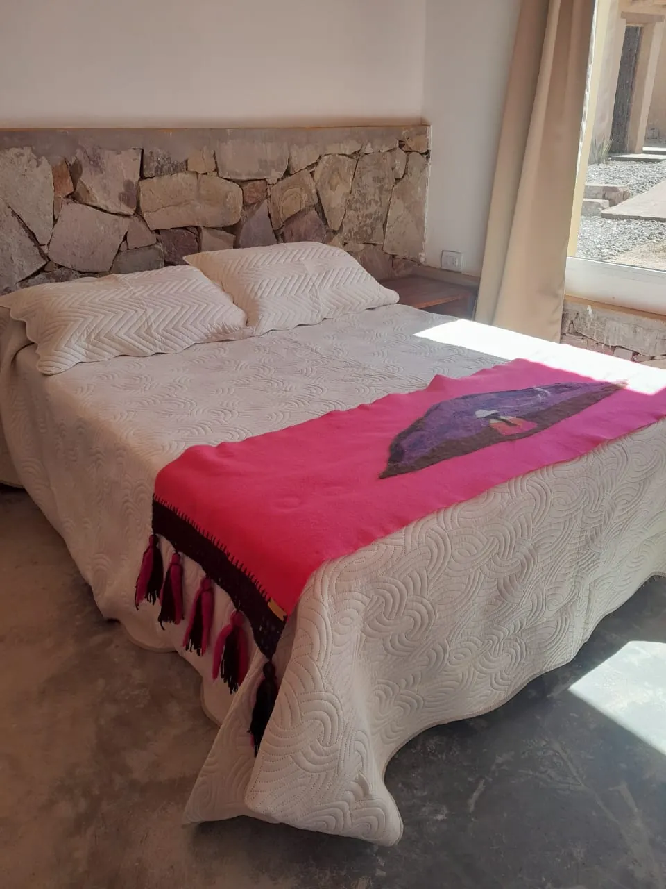Cabaña Agua: cama matrimonial con cabecera de piedra y pie de cama fucsia
