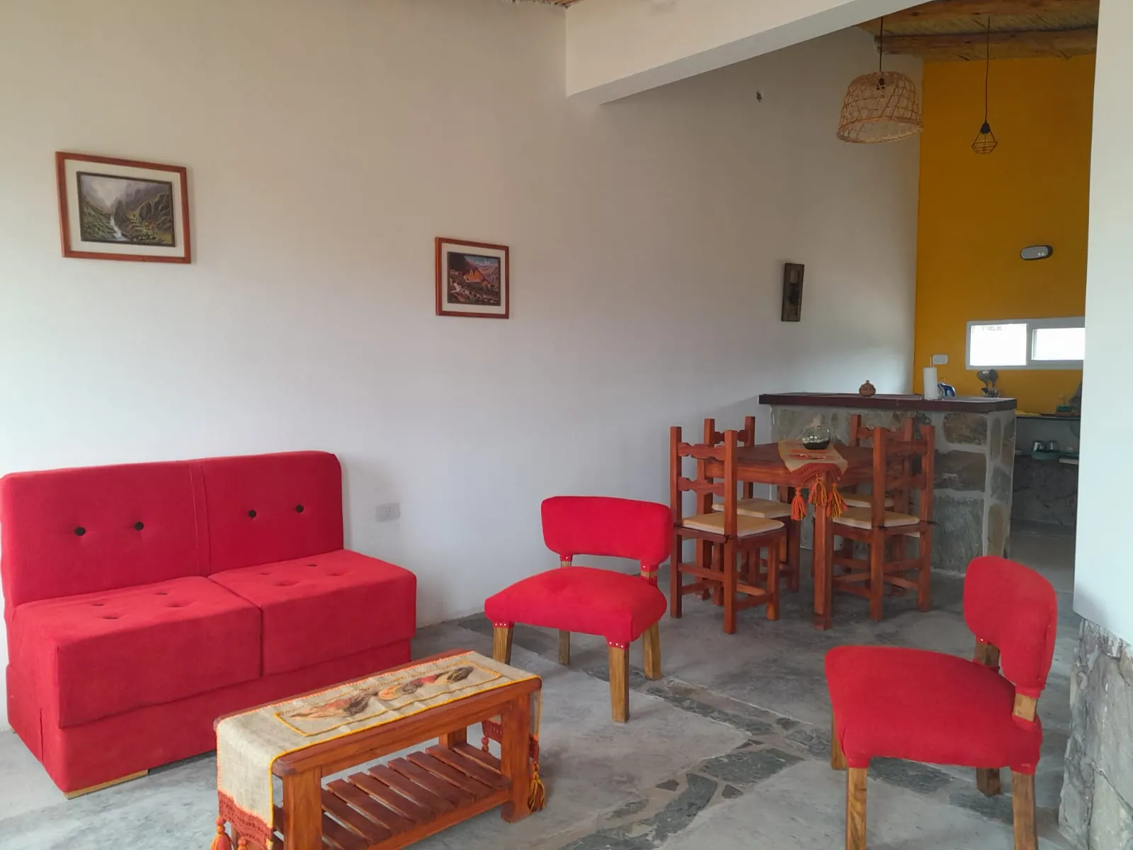 Cabaña Aire: living con sillones rojos, mesa ratona con telar y cocina con pared amarilla