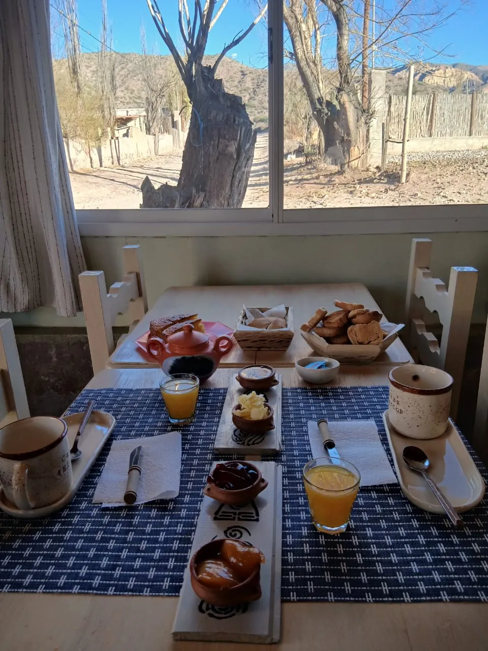Mesa de desayuno junto a la ventana, con pan casero, dulces y jugo de naranja