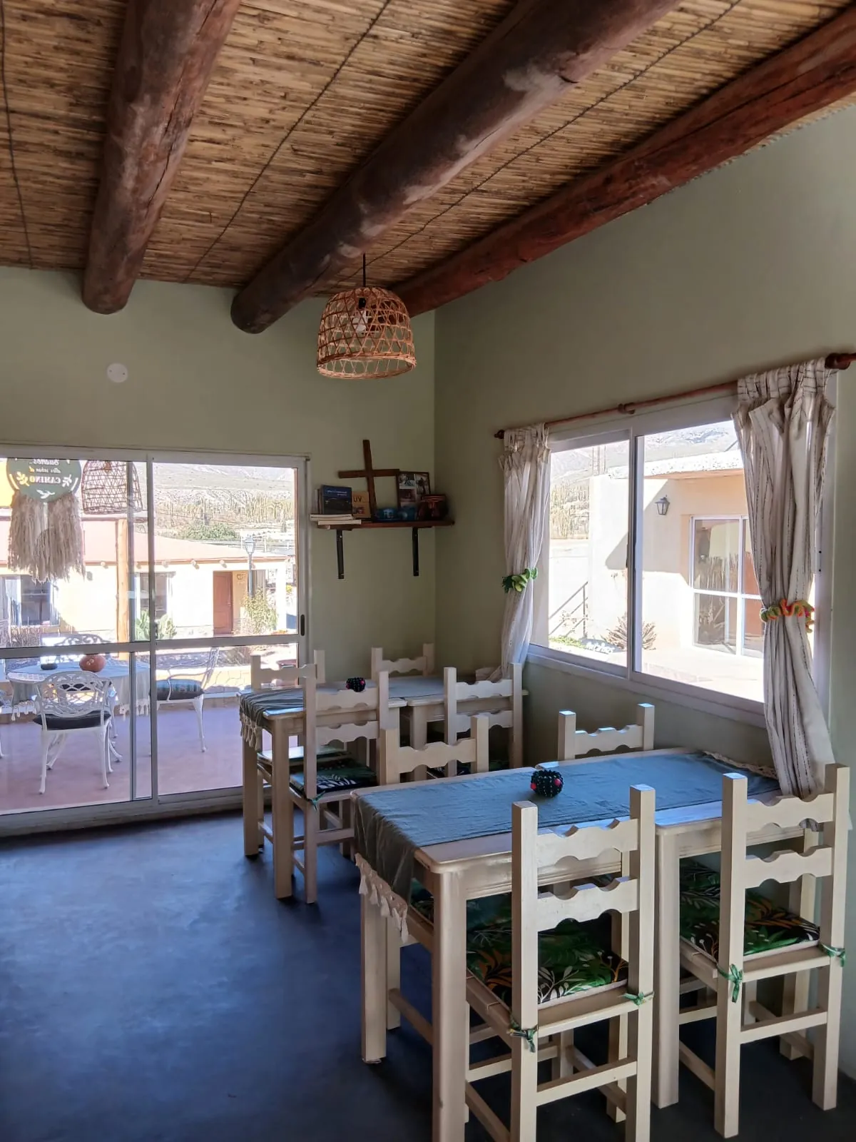 Salón desayunador con techo de caña, mesas de madera y ventanales al patio